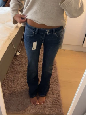 Mörkblå bootcut jeans med brodyr - Säljer ett par mörkblå bootcut jeans med snygg broderad detalj på bakfickan. Jeansen har låg midja, klassiska fem fickor och en cool tvättad look. Perfekta för dig som gillar en avslappnad men trendig stil. ⭐️Aldrig använda i med att jag vuxit ur dem