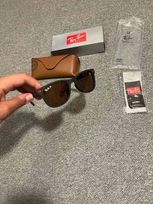 Svarta Ray-Ban Wayfarer solglasögon - Snygga svarta Ray-Ban Wayfarer solglasögon med klassisk form och mörka glas. Kommer med originalfodral, putsduk och box. Perfekta för att lyfta din stil med en ikonisk accessoar.