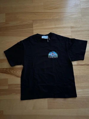 Svart t-shirt Casablanca - Snygg svart t-shirt Casablanca med färgglatt tryck och logga på bröstet. Klassisk rund hals och korta ärmar. Perfekt för dig som gillar stilrena plagg med en twist. Tillverkad i mjuk bomull för skön känsla hela dagen.