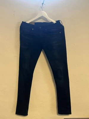 Dondup jeans Mörkblå - Säljer ett par mörkblå skinny jeans med klassisk femficksdesign och smal passform. Jeansen har knapp- och dragkedjestängning samt diskreta slitningar framtill för en trendig look. Perfekta till en avslappnad stil.