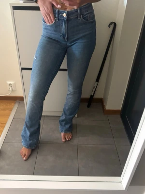 Blå bootcut jeans  - Säljer ett par ljusblå bootcut jeans. Jeansen har klassisk femficksmodell, hög midja och raka ben som går ut lite nertill. Perfekta till vardagslooken och sitter snyggt på kroppen. Materialet är denim i bomull.