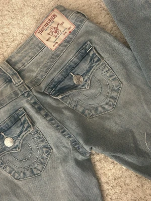 True Religion Joey Low Rise Flare Jeans - Snygga ljusblå jeans från True Religion, modell Joey med låg midja och utsvängda ben. Klassiska fickor med dekorativa sömmar och silverfärgade knappar! (Använda ca 3 gånger) 