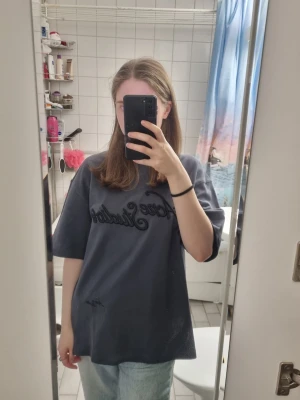 Oversized mörkgrå t-shirt från acne  - Säljer en oversized mörkgrå t-shirt med svart broderad text på bröstet. T-shirten har en loose passform och är kortärmad, perfekt för en avslappnad stil. Tillverkad i mjuk bomull som känns skön mot huden. Acne studios 