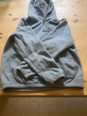 Grå hoodie från Levi's med huva - Säljer en enkel och stilren grå hoodie från Levi's. Hoodien har en klassisk huva med dragsko, magficka framtill och elastiska muddar vid ärmslut och nederkant. Tillverkad i mjukt material som känns skönt mot huden. Perfekt för en avslappnad look.