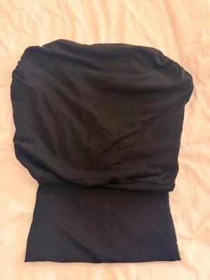 Svart axelbandslös tubtopp - Snygg svart axelbandslös tubtopp med bandeau-modell. Toppen har en enkel och clean design som passar perfekt till många olika outfits. Tillverkad i mjukt och stretchigt material för en bekväm passform.