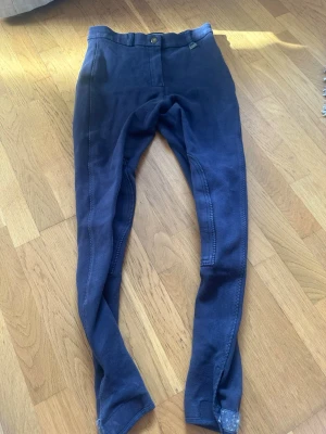 Mörkblå ridbyxor med kardborre - Mörkblå ridbyxor med förstärkta knän och kardborrestängning vid bensluten. Byxorna har en smal passform och är gjorda i ett stretchigt material som ger bra rörelsefrihet. Perfekta för ridning och annan hästsport. Har använt dom när jag var mindre men är fortfarande i fint skick. 