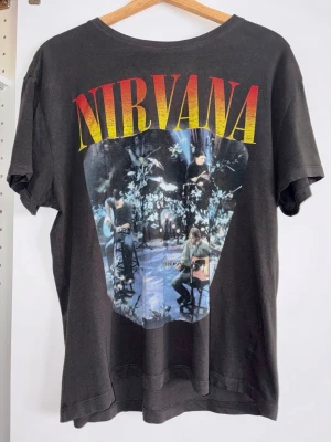 Svart t-shirt med Nirvana-tryck - Cool svart t-shirt med stort färgglatt Nirvana-tryck på framsidan och motiv från MTV Unplugged 1994. — T-shirten har rund hals och korta ärmar, perfekt för dig som gillar bandmerch och vill sticka ut med en ikonisk look. — Sparsamt använd, i mycket bra skick. — Inköpt på Carlings i märket Stay. — Nypris ca. 400 kr.