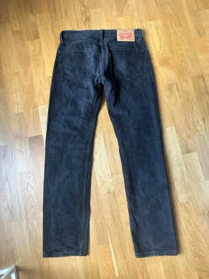 Svarta raka jeans från Levi's w28 l32 - Säljer ett par svarta jeans Levi's 505 med klassisk rak passform och fem fickor. Jeansen har en tydlig läderpatch bak i midjan och är tillverkade i kraftig denim. Perfekta för en avslappnad och stilren look.