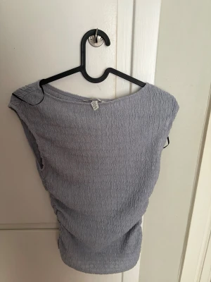 Ljuslila ribbad topp från H&M - Säljer en ljuslila ribbad topp från H&M i storlek XXS. Toppen är ärmlös och har en stretchig, vågig struktur som ger en snygg och modern look. Perfekt att matcha med jeans eller kjol för en trendig outfit.