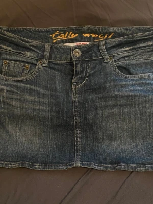 Mörkblå jeanskjol - Säljer en snygg mörkblå jeanskjol från Tally Weijl med klassisk femficksdesign, bälteshällor och knappstängning framtill. Kjolen har en kort modell och är gjord i slitstarkt denimtyg. Perfekt till en avslappnad och trendig look.