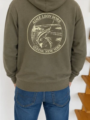 Olivgrön hoodie Aimé Leon Dore x woolrich - Snygg olivgrön hoodie från Aimé Leon Dore med stor grafisk print på ryggen och liten broderad detalj framtill. Klassisk känguruficka, ribbade muddar och justerbar huva. Perfekt för en avslappnad streetwear-look.OBS finns en lite fläck under magfickan men den synns knapps