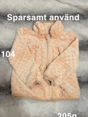 Ljusrosa pluppfleece - Supermjuk ljusrosa pluppfleece med dragkedja och huva. Fleecen har ett bubbligt prickmönster i tyget och ribbade muddar vid ärmsluten. Perfekt för dig som gillar mysiga och trendiga plagg.🌸 Sparsamt använd. Storlek 104