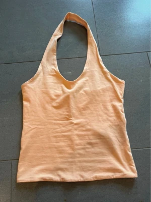 Ljus orange halterneck linnetopp XS - Säljer en ljus orange halterneck linnetopp från Gina Tricot i storlek XS. Toppen är ärmlös och har en djup urringning med smala axelband som knyts i nacken. Perfekt till sommaren och enkel att styla med jeans eller kjol.