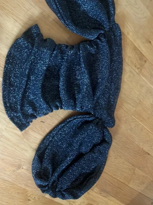 Glittrig offshoulder topp svart XS - Supersnygg svart offshoulder topp med glittereffekt. Toppen har puffiga ärmar och en croppad passform som ger en trendig look. Perfekt för dig som vill sticka ut med lite extra glans. Materialet är stretchigt och bekvämt.