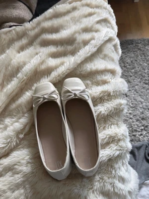 Beige ballerinaskor med rosett - Snygga beige ballerinaskor med rund tå och dekorativ rosett framtill. Skorna har en diskret struktur på tån och är gjorda i ett material som liknar konstläder. Passar perfekt till jeans eller klänning för en stilren look.