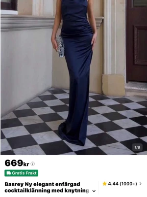 Marinblå långklänning med slits - Oanvänd snygg marinblå långklänning med hög hals och öppen rygg. Klänningen har en elegant slits på sidan och är ärmlös, vilket ger en stilren och modern look. Perfekt för dig som vill sticka ut på festen.