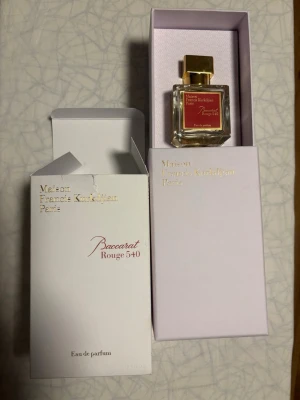 Maison Francis Kurkdjian Baccarat Rouge 540 - Lyxig parfymflaska Baccarat Rouge 540 från Maison Francis Kurkdjian. Flaskan är fyrkantig i genomskinligt glas med guldfärgad kork och röd etikett med gulddetaljer. Kommer i elegant vit och ljusrosa förpackning med guldfolierad text.