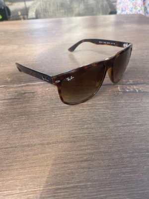 Bruna solglasögon från Ray-Ban - Snygga solglasögon från Ray-Ban med klassisk fyrkantig form och brunmelerad båge. Glasen är mörka och ger ett coolt intryck. Perfekta för soliga dagar och ger en tidlös vibe till din outfit.