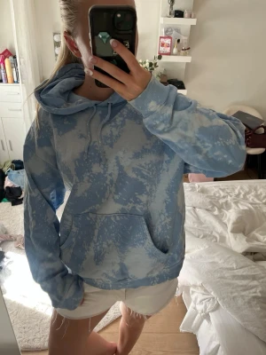 Blå tie-dye hoodie från Monki - Säljer en blå och vit tie-dye hoodie från Monki i storlek S. Hoodien har en stor huva med dragsko, magficka och mjukt fleecefoder på insidan. Perfekt för dig som gillar en avslappnad och trendig stil.