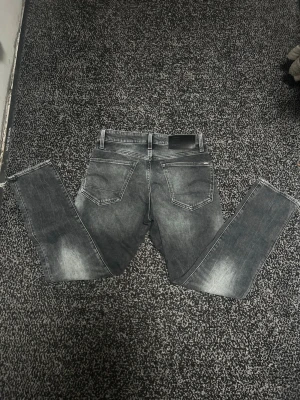 Grå slim fit jeans från G-Star RAW - Snygga grå slim fit jeans från G-Star RAW med slitna detaljer och klassiska bakfickor. Jeansen har en tvättad look och är tillverkade i mjukt denimtyg. Perfekta för dig som gillar en modern och avslappnad stil.