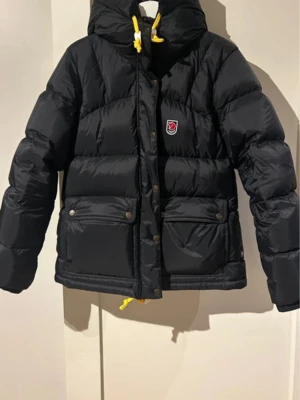 Svart dunjacka med huva från Fjällräven - I princip helt ny Fjällräven Expedition down lite i färgen svart och storlek M. Nypris 7500kr. Köpt på Team Sportia. Perfekt för kalla vinterdagar 