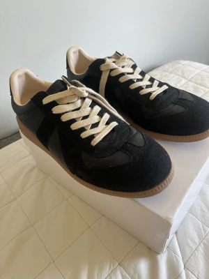 Svarta sneakers med beige sula - Säljer ett par stilrena svarta sneakers med beige sula och vita snören. Skorna har en klassisk låg modell med ovandel i mocka och läderdetaljer. Insidan är ljus och sulan är i gummi för bra grepp. Perfekta för en clean och avslappnad look.