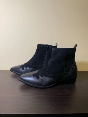 River Island Svarta cowboy boots i mocka och äkta skinn, stl 40 - Stilrena svarta cowboy boots med spetsig tå och låg klack. Bootsens ovandel är i mocka med detaljer i slätt skinn och dekorativa sömmar. Dragkedja på insidan för enkel påtagning och klassisk westerninspirerad look. Äkta skinn och mocka, stl 40, nya oanvända 