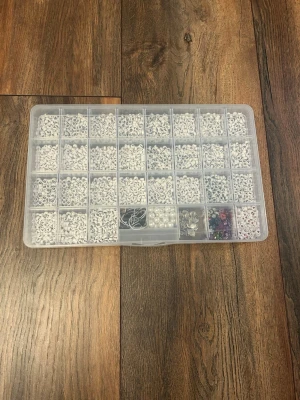 Stor ask med bokstavspärlor - Säljer en stor plastask fylld med vita bokstavspärlor i svart text, några pärlor i färg samt pärlor som ser ut som pärlor och några berlocker. Perfekt för att göra egna smycken som armband och halsband. Innehåller även elastisk tråd.