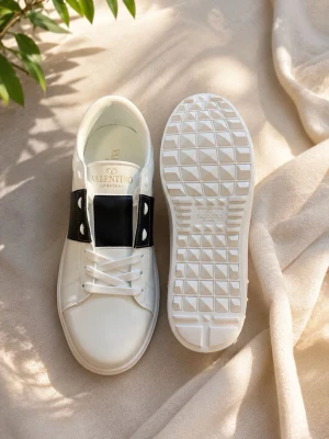 Valentino opens  - Snygga vita sneakers från Valentino Garavani med bred svart läderdetalj över snörningen och coola nitar på hälen. Skorna har en chunky vit sula med rutmönster undertill och är tillverkade i slätt läder. Perfekta för dig som gillar stilrena men ändå unika sneakers. Kommer med box