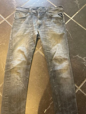 Grå slim fit jeans med slitningar - Säljer ett par grå slim fit jeans med snygga slitningar och tvättade detaljer. Jeansen har fem fickor, normal midja och raka ben. Materialet är klassisk denim med stretch för extra komfort. Perfekta för en avslappnad och trendig look.
