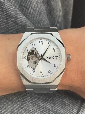 XoR Silver klocka Automatiskt Urverk - Stilren klocka från XoR med silverfärgat armband i metall och en unik öppen urtavla som visar urverket. Klockan har ett automatiskt Urverk. Urtavlan har arabiska siffror och en modern, kantig form. Perfekt för dig som gillar detaljer och mekanik. HELT NY!