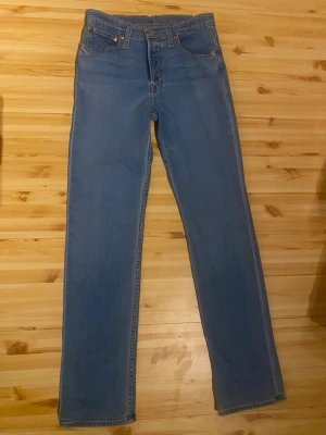 Ljusblå raka jeans från Levi's - Säljer ett par klassiska ljusblå jeans från Levi's med rak passform och hög midja. Jeansen har fem fickor, gylf med knappstängning och Levi's ikoniska läderpatch bak i midjan. Perfekta till en avslappnad stil och tillverkade i slitstark denim. 