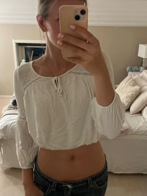 Vit croppad blus med knyt - Säljer en söt vit croppad blus med långa ärmar och knyt framtill. Blusen har fina spetsdetaljer vid axlar och ärmar samt en luftig passform. Perfekt till jeans eller kjol för en fräsch look💗 