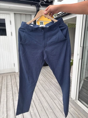 Mörkblå linnebyxor/chinos med smal passform Jack & Jones - Snygga mörkblå linnechinos med smal passform och klassiska sidfickor fram samt två bakfickor med knapp. Byxorna har bälteshällor och stängs med knapp och dragkedja. Tillverkade i ett lätt och bekvämt tyg som passar perfekt till en avslappnad stil. 