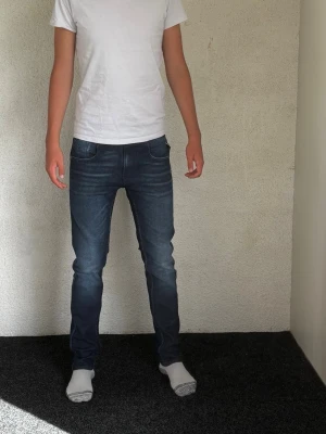 Mörkblå slim fit jeans herr replay  - Säljer ett par mörkblå slim fit jeans med klassisk femficksdesign och lätt slitningar på låren. Jeansen har normal midja och smal passform hela vägen ner. Perfekta till en avslappnad stil och passar till det mesta. Materialet är stretchigt denim för extra komfort.