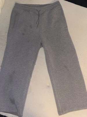 Gråa mjukisbyxor med raka ben - Ett par klassiska grå mjukisbyxor från Weekday med raka ben och dragsko i midjan. Byxorna har två sidofickor fram och en bakficka. Tillverkade i mjukt sweatshirtmaterial som är perfekt för chill dagar hemma eller när du vill vara extra bekväm.  Defekter som synliga på bilden. Går förmodligen att få bort fläckarna med hjälp av en färg korrigerande sprej.