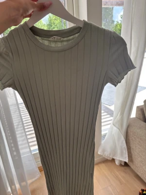 Ljusgrön ribbad kortklänning - Kort, ribbad klänning i ljusgrönt med rund halsringning och korta ärmar. Klänningen har en kroppsnära passform och är tillverkad i ett mjukt, stretchigt material som känns bekvämt mot huden. Perfekt för varma dagar och enkel att styla.