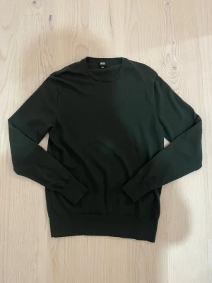 Mörkgrön stickad tröja Uniqlo - En stilren mörkgrön stickad tröja från Uniqlo med rund halsringning och långa ärmar. Tröjan har ribbade muddar vid ärmslut och nederkant. Perfekt basplagg i mjukt material som passar till det mesta.