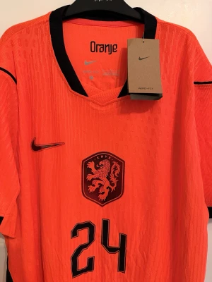 Holland hemmatröja 25/26 - Säljer en authentic orange Holland fotbollströja från Nike med svart detaljering, nummer 24 och namnet Summerville på ryggen. Tröjan är mycket fin och skön med fina detaljer.
