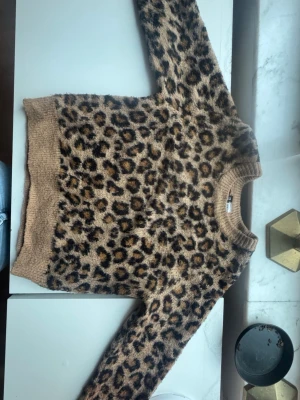 Leopardmönstrad stickad tröja H&M XS - Säljer en supermjuk stickad tröja från H&M i storlek XS. Tröjan har ett snyggt leopardmönster i beige, brunt och svart samt ribbade muddar vid hals, ärmslut och nederkant. Perfekt för dig som vill ha en trendig och bekväm look.(pris kan diskutera)