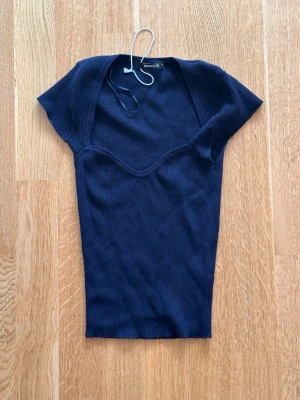 Mörkblå ribbad topp med v-ringning - Mörkblå ribbad topp med korta ärmar och snygg v-ringning. Toppens material är stretchigt och sitter figurnära. Perfekt att styla med jeans eller kjol för en trendig look.