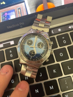 Swatch klocka - Stilren Swatch med blå urtavla och silverfärgade detaljer. Klockan har tre subdials, datumvisning och robust länkarmband i rostfritt stål. Perfekt accessoar för dig som gillar klassisk men sportig stil. Klockan är Otestad då jag ej har batteri att testa med och nuvarande batteri är urladdat