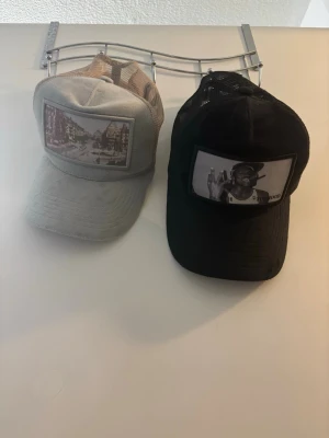 Garavelli och Tophood keps bundle - Säljer två kepsar med mesh-bakstycke och broderad text på sidan. Ena kepsen är beige med stadsmotiv framtill och texten 'GARAVELLI' på sidan. Den andra är svart med foto-tryck framtill och texten 'TOPHOOD' på sidan. Perfekt för en streetwear-look.