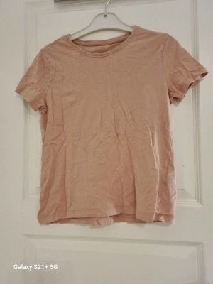 Rosa basic t-shirt - En enkel och stilren rosa  t-shirt  i mjuk bomull. T-shirten har rund halsringning och korta ärmar, perfekt för en avslappnad look. Passformen är normal och tyget är tunt och skönt mot huden.