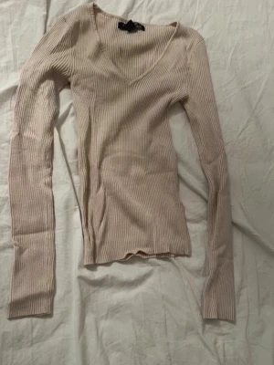 Beige ribbad stickad tröja - Säljer en beige ribbad stickad tröja från Amisu i storlek XS. Tröjan har lång ärm och djup v ringning. 