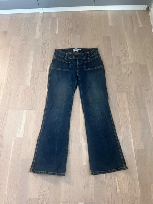 Mörkblå low bootcut jeans  - Snygga mörkblå bootcut jeans med två stora fickor fram och klassiska bakfickor. Jeansen har låg midja och utsvängda ben. Materialet är denim i bomull med kontrastsömmar. Perfekta för en trendig och avslappnad stil.