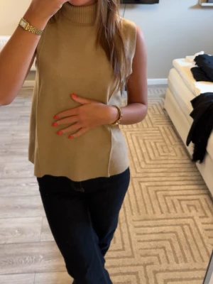 Beige ärmlös polotopp - Säljer en beige ärmlös polotopp i mjukt material. Toppen har hög krage och en loose passform som ger en avslappnad look. 