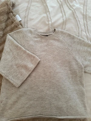 Beige stickad tröja Gina Tricot - Mysig beige stickad tröja från Gina Tricot med rund halsringning och avslappnad passform. Tröjan har långa ärmar och ribbade muddar vid halsen. Perfekt för lager på lager under kyliga dagar.