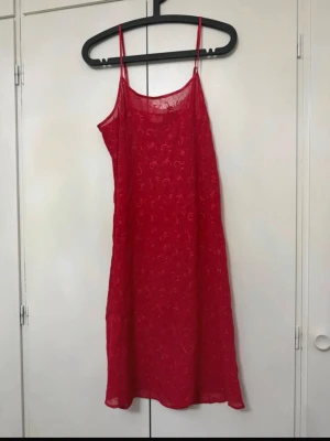 Rött nattlinne - Säljer ett rött nattlinne med tunna axelband och lätt transparent tyg. Nattlinnet har en rak passform och är dekorerat med ett subtilt mönster i tyget. Perfekt för en bekväm och stilren look på kvällen.