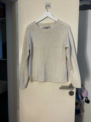 Beige stickad tröja i ullmix - Mysig beige stickad tröja med rund hals och långa ärmar. Tröjan har en enkel och stilren design med ribbade muddar vid ärmslut och nederkant. Materialet känns mjukt och värmande, perfekt för kyliga dagar. Lite knottrig annars bra